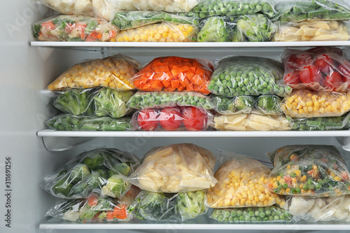Plastic bags with different frozen vegetables in refrigerator photo