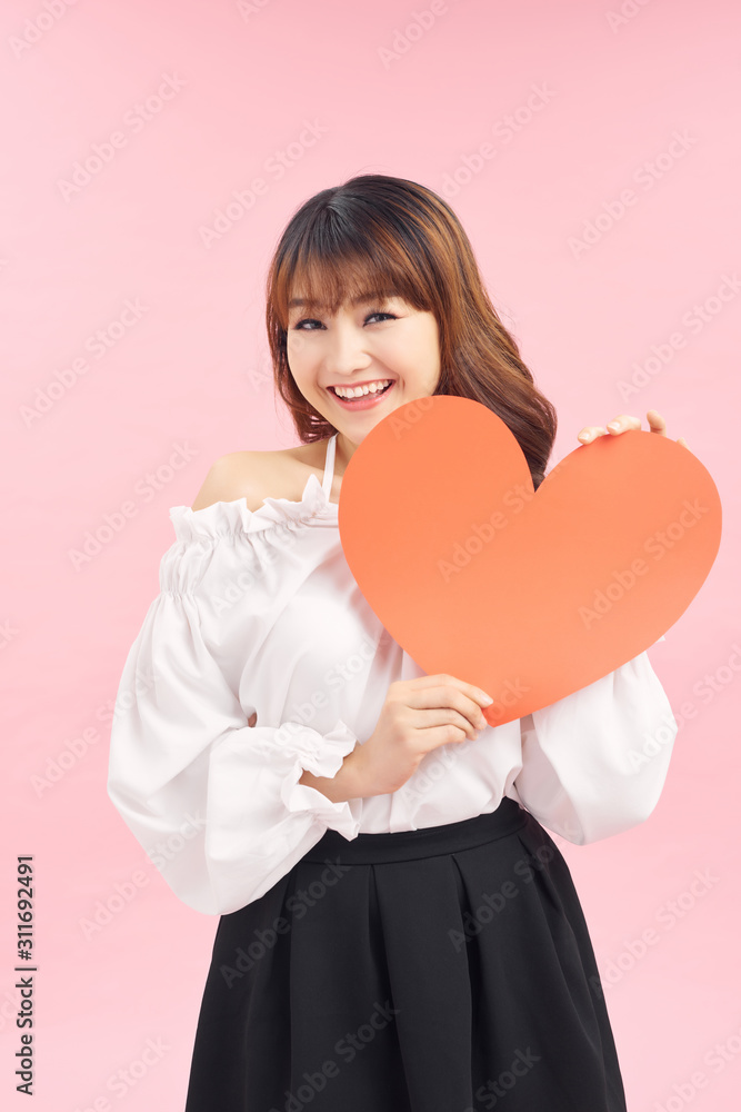 Cute asian woman holding red heart isolated on pink Cute asian woman holding red heart isolated on pink