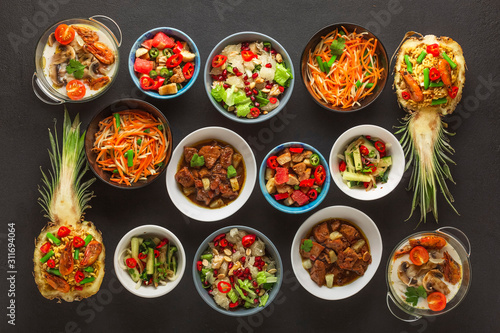 Assortment of Thai cooked dishes in bowls on a black concrete background. Top view.