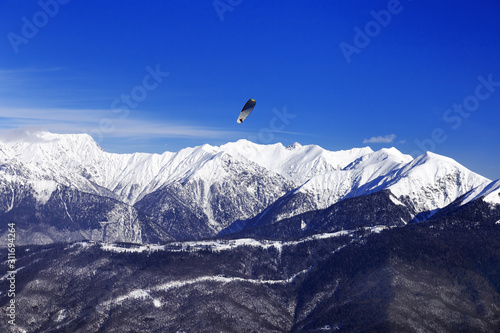 Beautiful environmental view of Caucasus mountain range and paraglider soaring in air. Rosa Khotor ski resort. Blue sky and high mountains covered snow.