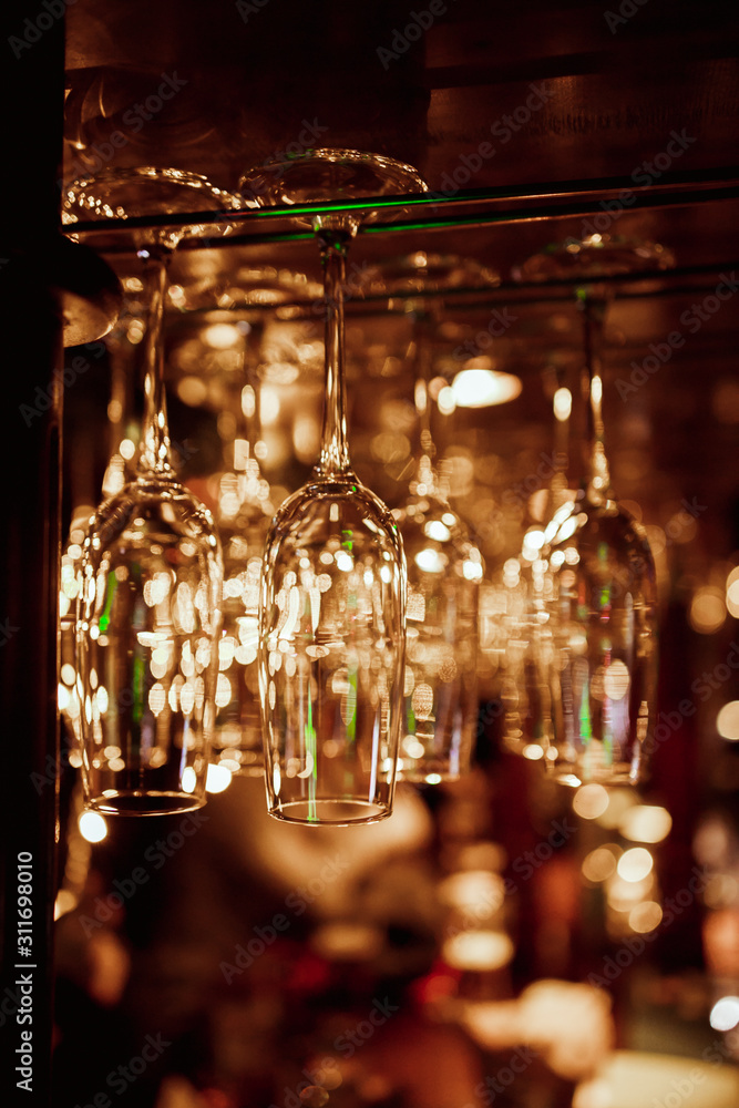 Glasses of wine. Glasses hanging above the bar in the restaurant. Empty glasses for wine. Wine and martini glasses in shelf above a bar rack in restaurant. blue lights, blue background, night life Glasses of wine. Glasses hanging above the bar in the restaurant. Empty glasses for wine. Wine and martini glasses in shelf above a bar rack in restaurant. blue lights, blue background, night life