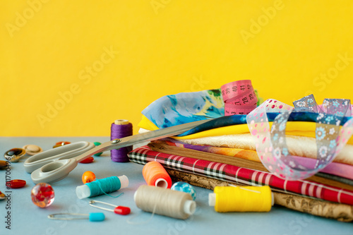 Accessories for sewing on a yellow background. Fabric, tailoring scissors, spools of thread, buttons for sewing clothes. There is space for text. Items for sewing.