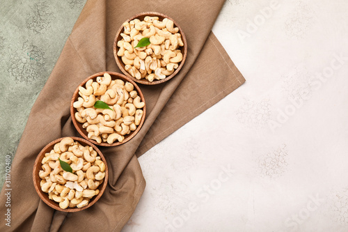 Bowls with tasty cashew nuts on color background