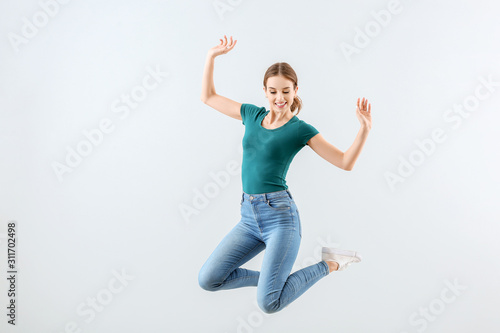 Jumping young woman against light background
