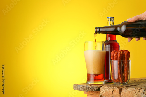 Composition with fresh beer and sausages on table against color background
