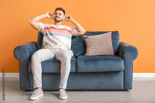Young man listening to music while sitting on sofa at home © Pixel-Shot
