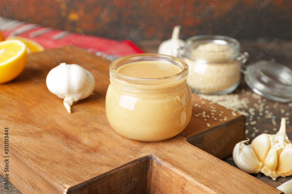 Jar of tasty tahini on wooden board Jar of tasty tahini on wooden board