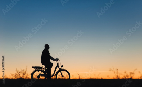 Male cyclist on the e-bike or electric bicycle on the sunset background. Silhouette of the man in profile. Active pension. Travel. Sport.