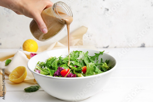Fotografia Woman pouring tasty tahini from jar onto vegetable salad in bowl