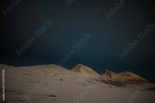 Dramatic night with many clouds and stars on the sky over the mountains in the North of Europe - Tromso, Norway. Star tracks. long shutter speed. © Tatiana