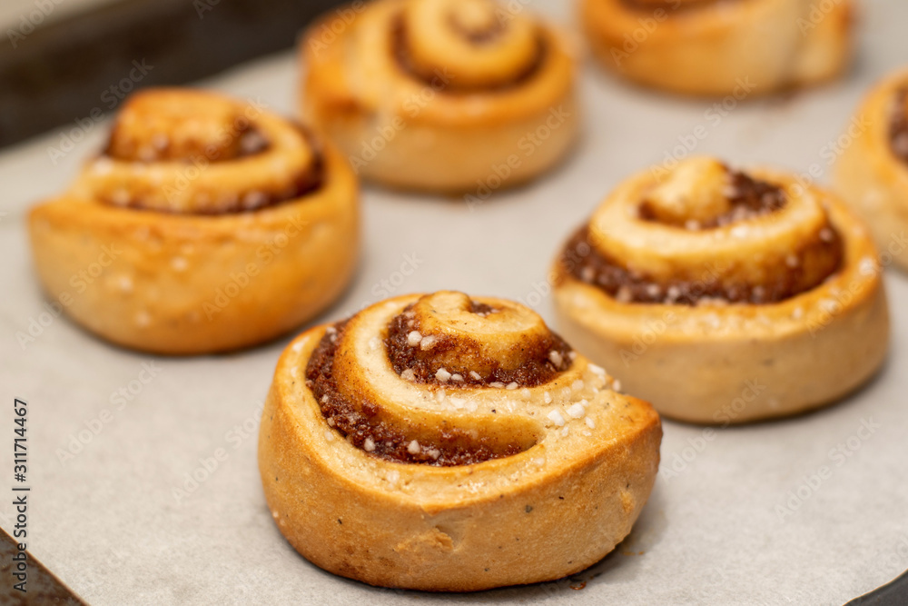 Freshly baked cinnamon buns rolls on a tray lined with baking parchment paper Freshly baked cinnamon buns rolls on a tray lined with baking parchment paper