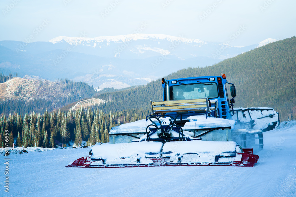 Snow blower machine working in ski resort with forest and mountains at background Snow blower machine working in ski resort with forest and mountains at background