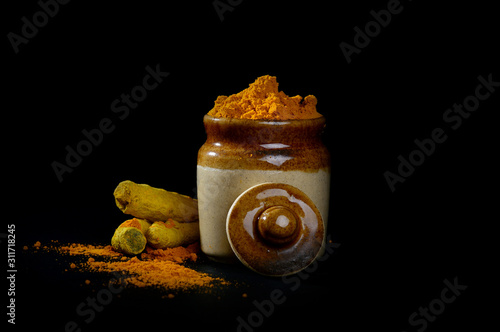 Turmeric powder in clay pot with roots or barks on black background photo