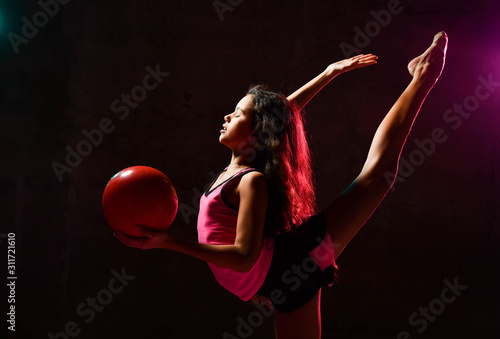 Young slim athletic girl gymnast doing gymnastic exercises stretching with ball in her hand in neon lights © Dmitry Lobanov
