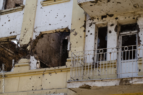 Destroyed building after hostilities. Photo of the destroyed building, the theme of the war. Military actions. Wall with holes in several places. Crumbling wall of hostilities.
