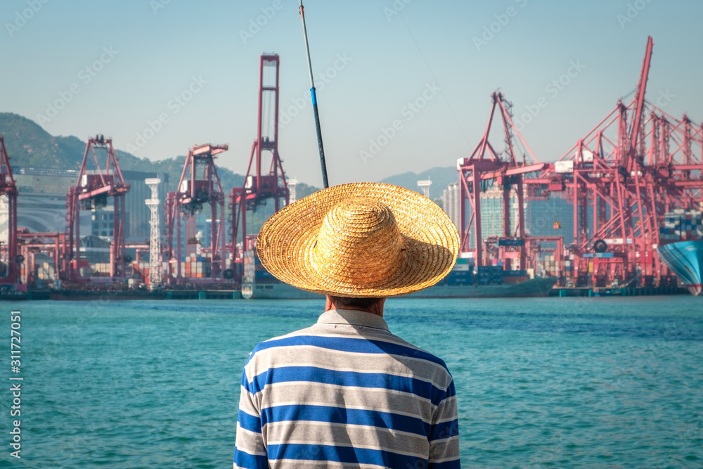 Fisher man with fishing rod from behind near container ship and freight harbour in HongKong