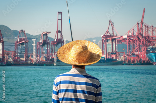 Canvas Print Fisher man with fishing rod from behind near container ship and freight harbour