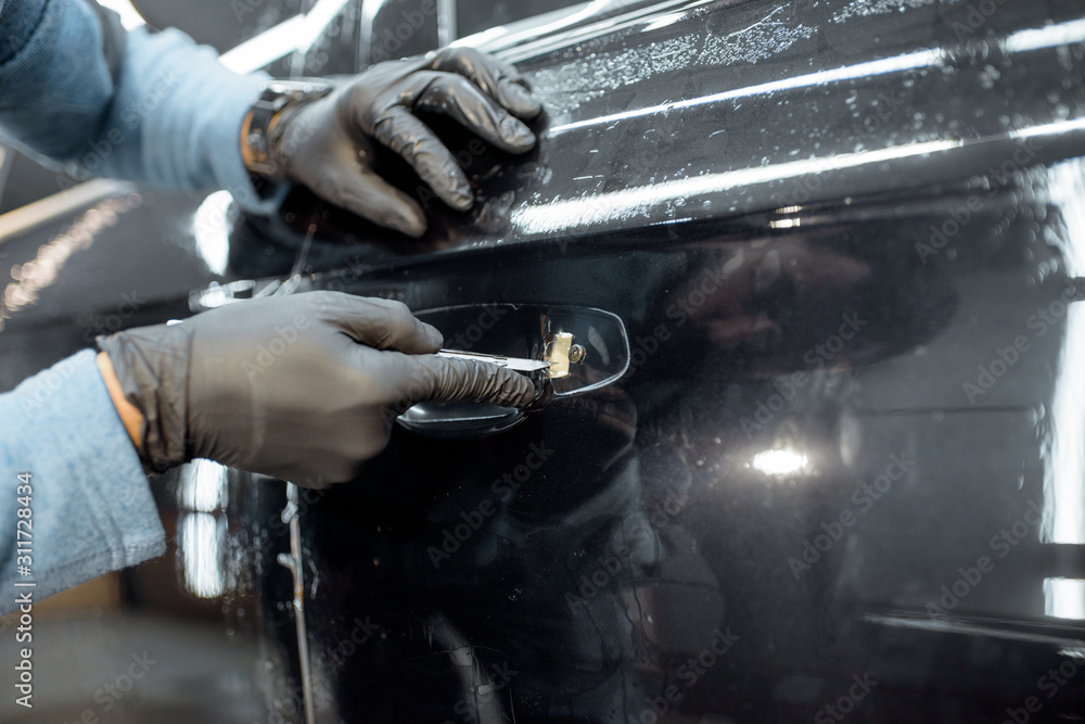 Obraz premium Worker sticking protective transparent film on a car body in place of the door handle, close-up view