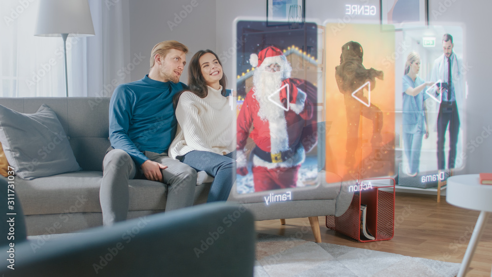 Beautiful Young Couple are Sitting on a Couch at Home and Choosing a Movie to Watch on a Futuristic Hologram Screen.