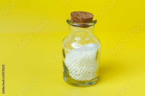 Classical Homeopathy globules and vintage glass bottles on yellow background. Alternative Homeopathy medicine herbs, healtcare and pills concept. Place for text.