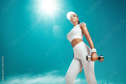 Sporty and fit woman athlete doing training with dumbbells on the sky background. The concept of a healthy lifestyle and sport. Individual sports recreation.