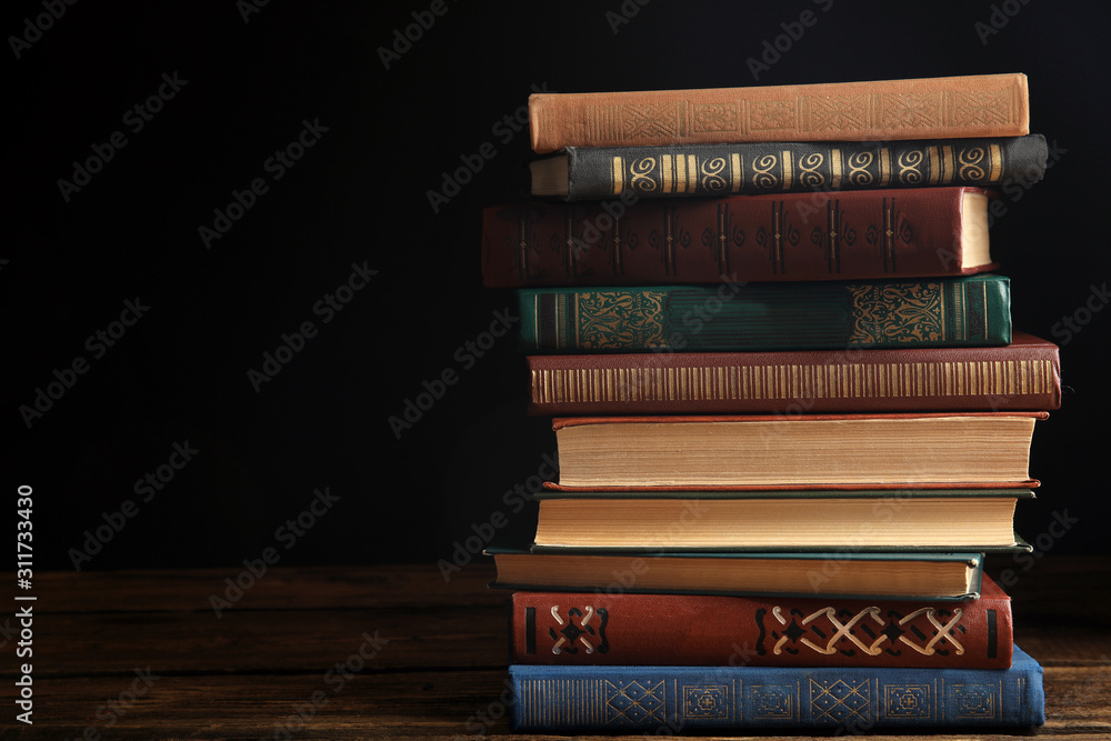 Collection of different books on wooden table against dark background. Space for text Collection of different books on wooden table against dark background. Space for text