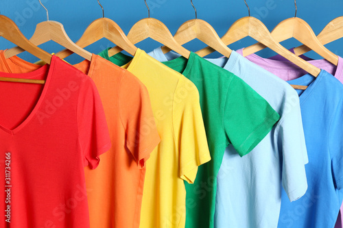 Bright clothes on wooden hangers against blue background. Rainbow colors