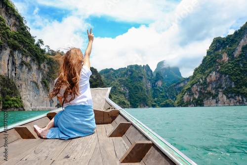 Vacation planing and travel holiday concept, Young woman traveler relaxing and sitting on the boat and look around island among reservoir , Tourist on summer at Cheow Lan Dam in Thailand
