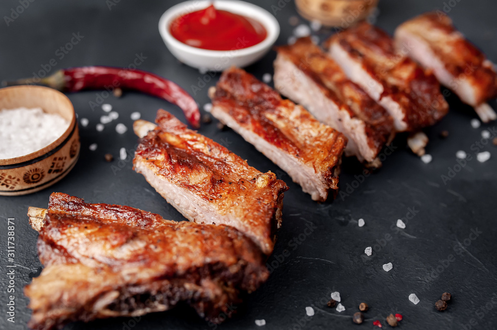 grilled pork ribs with spices and ketchup on a stone background