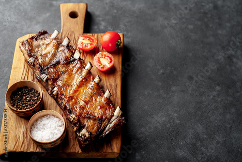 grilled pork ribs on a cutting board with spices on a stone background with copy space for your text