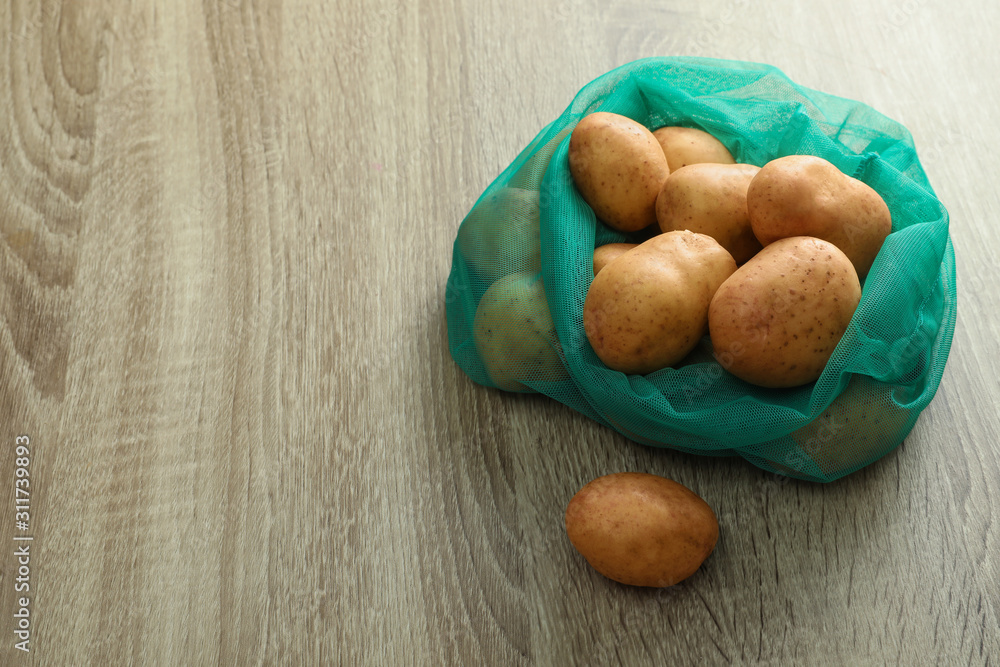 Net bag with potatoes on wooden table. Space for text Net bag with potatoes on wooden table. Space for text