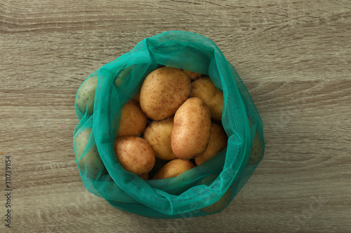 Net bag with potatoes on wooden table, top view