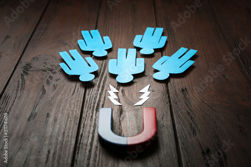 Magnet attracting paper people on wooden background