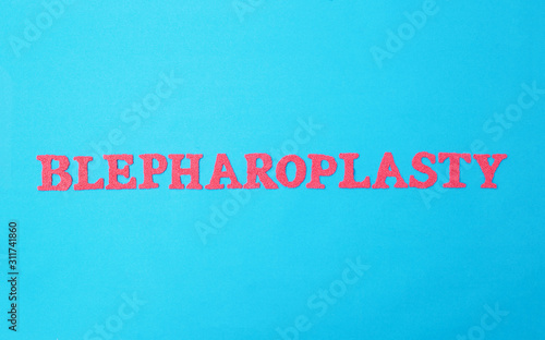 Word blepharoplasty in red letters on a blue background. The concept of plastic surgery involved in lifting the skin of the lower and upper eyelids, removing swelling and wrinkles around the eyes, photo