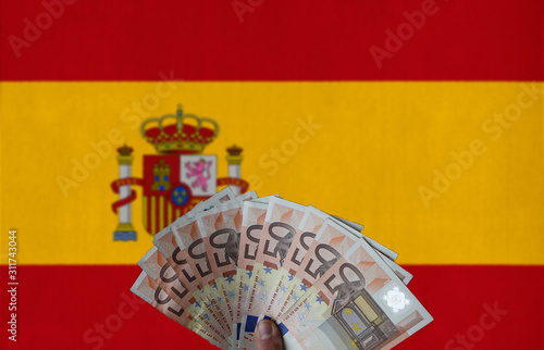 Spain flag with Euro banknotes in the hand