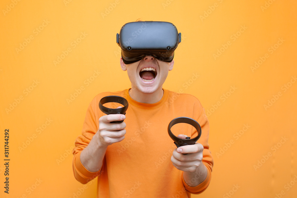 guy in VR glasses on an orange background, a gamer plays a virtual game and screams