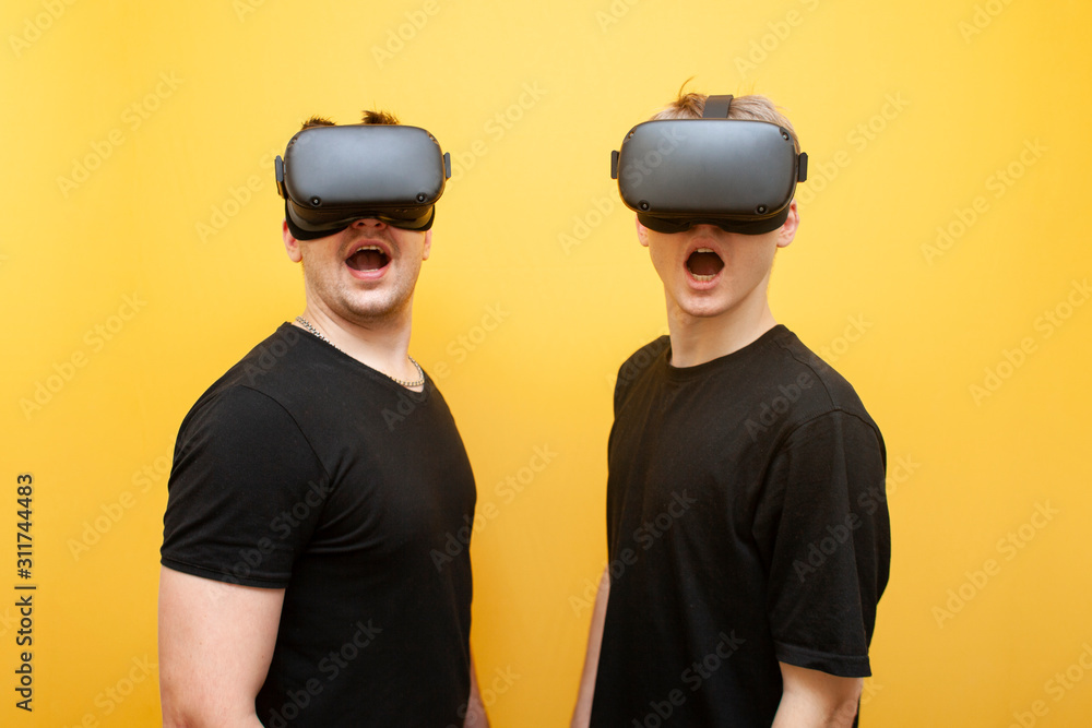 two surprised guys in VR glasses on a yellow background, a pair of friends of gamers in virtual reality glasses two surprised guys in VR glasses on a yellow background, a pair of friends of gamers in virtual reality glasses