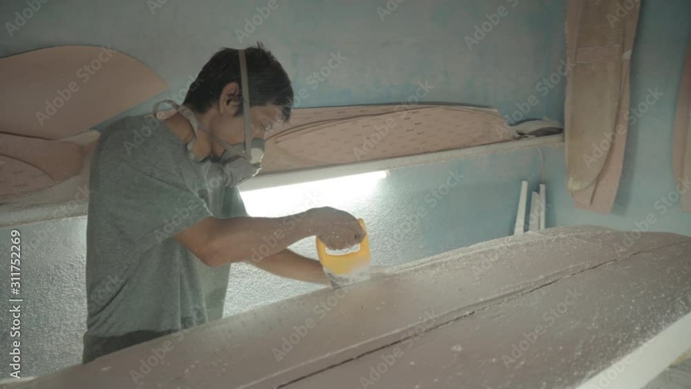 Sequence of shots of Asian woodworker wearing safety respirator sawing surfboard blank using handsaw Sequence of shots of Asian woodworker wearing safety respirator sawing surfboard blank using handsaw
