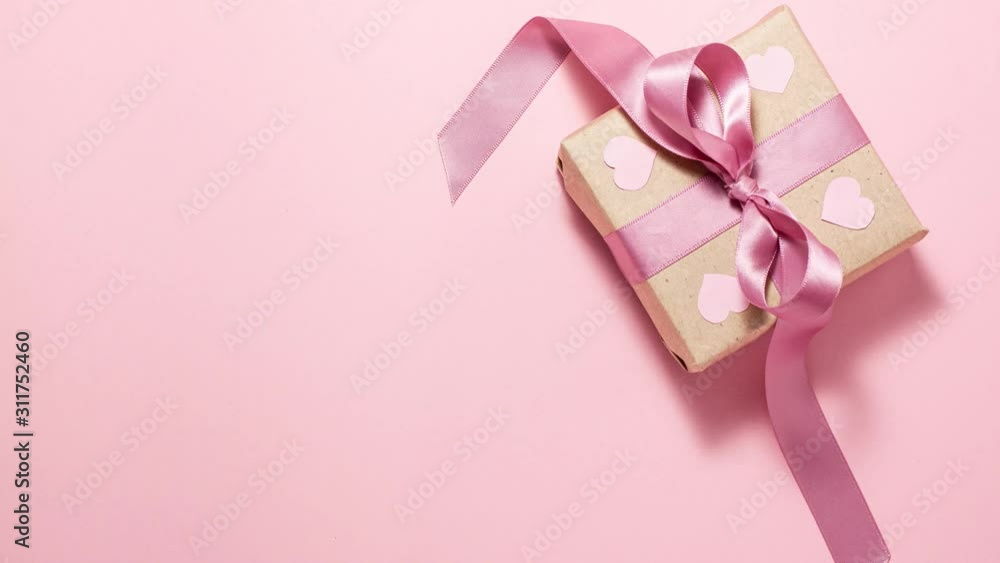 Gift box with a purple ribbon bow and four pink hearts are in the frame on pink background. Valentines day concept. Flat lay top view stop motion animation with space for text Gift box with a purple ribbon bow and four pink hearts are in the frame on pink background. Valentines day concept. Flat lay top view stop motion animation with space for text