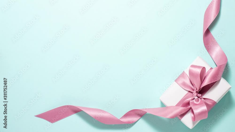 White gift box with a purple ribbon bow are in the frame on blue background. Valentines day concept. Flat lay top view stop motion animation with space for text White gift box with a purple ribbon bow are in the frame on blue background. Valentines day concept. Flat lay top view stop motion animation with space for text