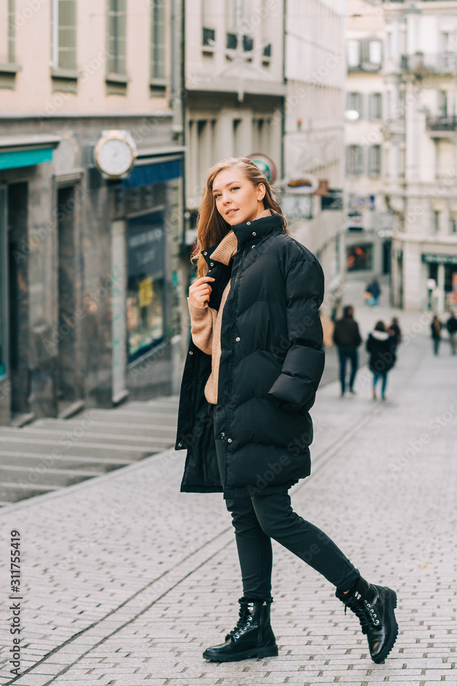 Street fashion portrait of young beautiful woman wearing beige roll neck pullover and black padded coat