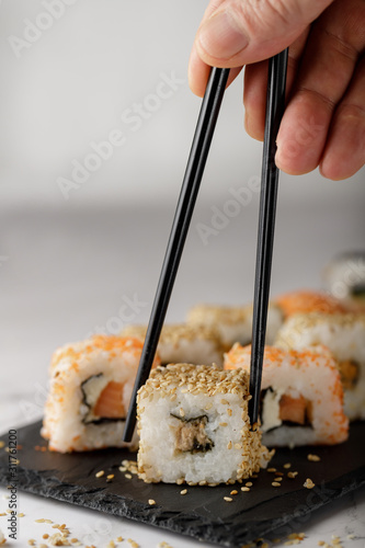Sushi with chopsticks. A man takes sushi with chopsticks from the board
