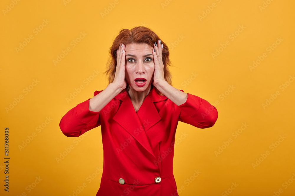 Shocked caucasian young woman keeping hands on cheeks, looking confused wearing fashion red jacket over isolated orange background. People lifestyle concept. Shocked caucasian young woman keeping hands on cheeks, looking confused wearing fashion red jacket over isolated orange background. People lifestyle concept.