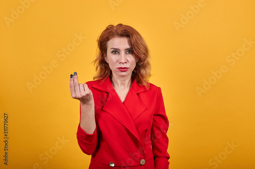 Disappointed caucasian young woman keeping fingers together, looking at camera wearing fashion red jacket over isolated orange background. People lifestyle concept.