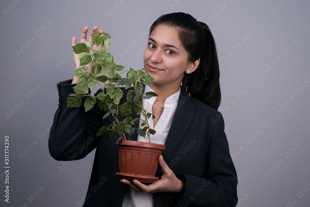 Portrait of a beautiful Indian young business woman in a business suit, holding a green indoor flower in her hand, smiling, rubbing it. Business profit growth concept Portrait of a beautiful Indian young business woman in a business suit, holding a green indoor flower in her hand, smiling, rubbing it. Business profit growth concept