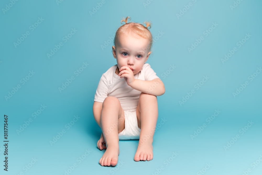 baby girl sits on the floor and sucks a finger