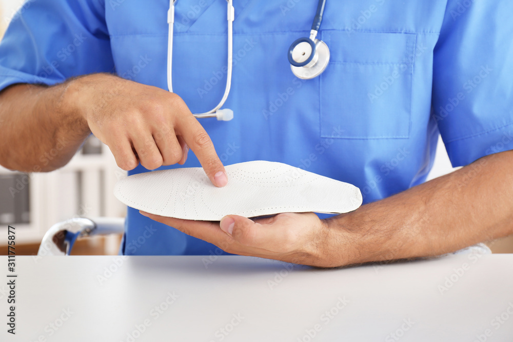 Male orthopedist showing insole in clinic, closeup