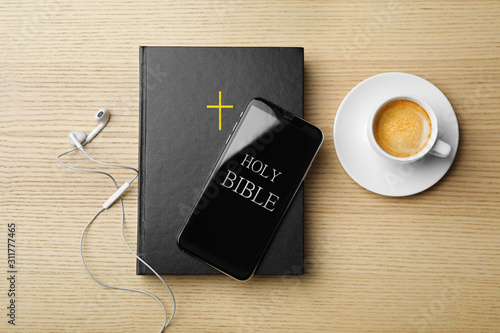 Bible, phone, cup of coffee and earphones on wooden background, flat lay. Religious audiobook