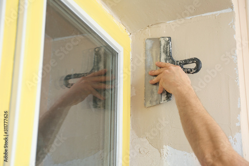 Man plastering window area with putty knife indoors, closeup. Interior repair photo