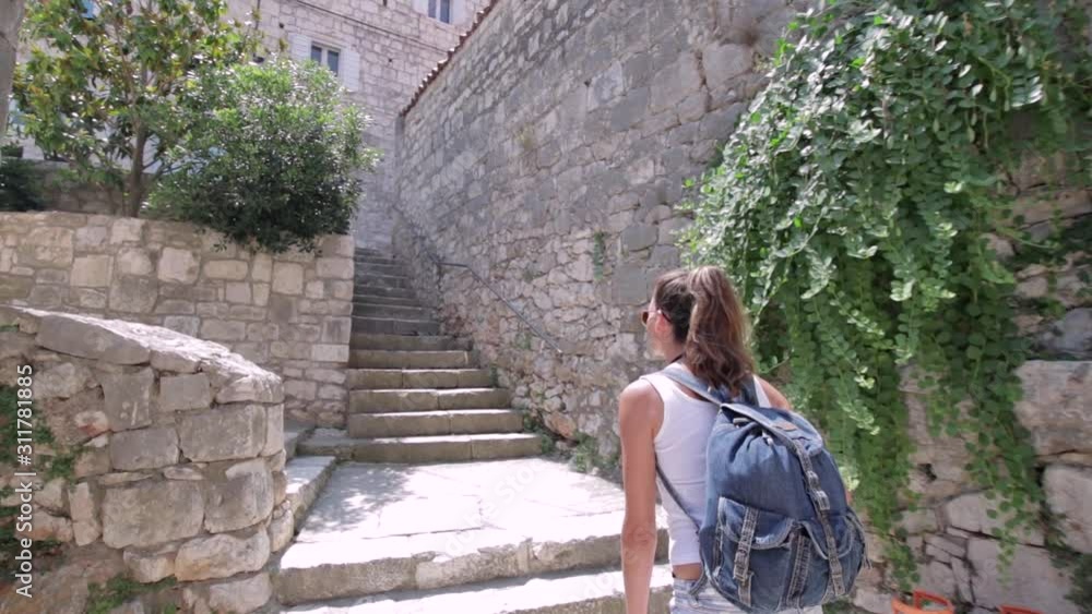 Young woman with a backpack climbing the stairs at old town Hvar Young woman with a backpack climbing the stairs at old town Hvar
